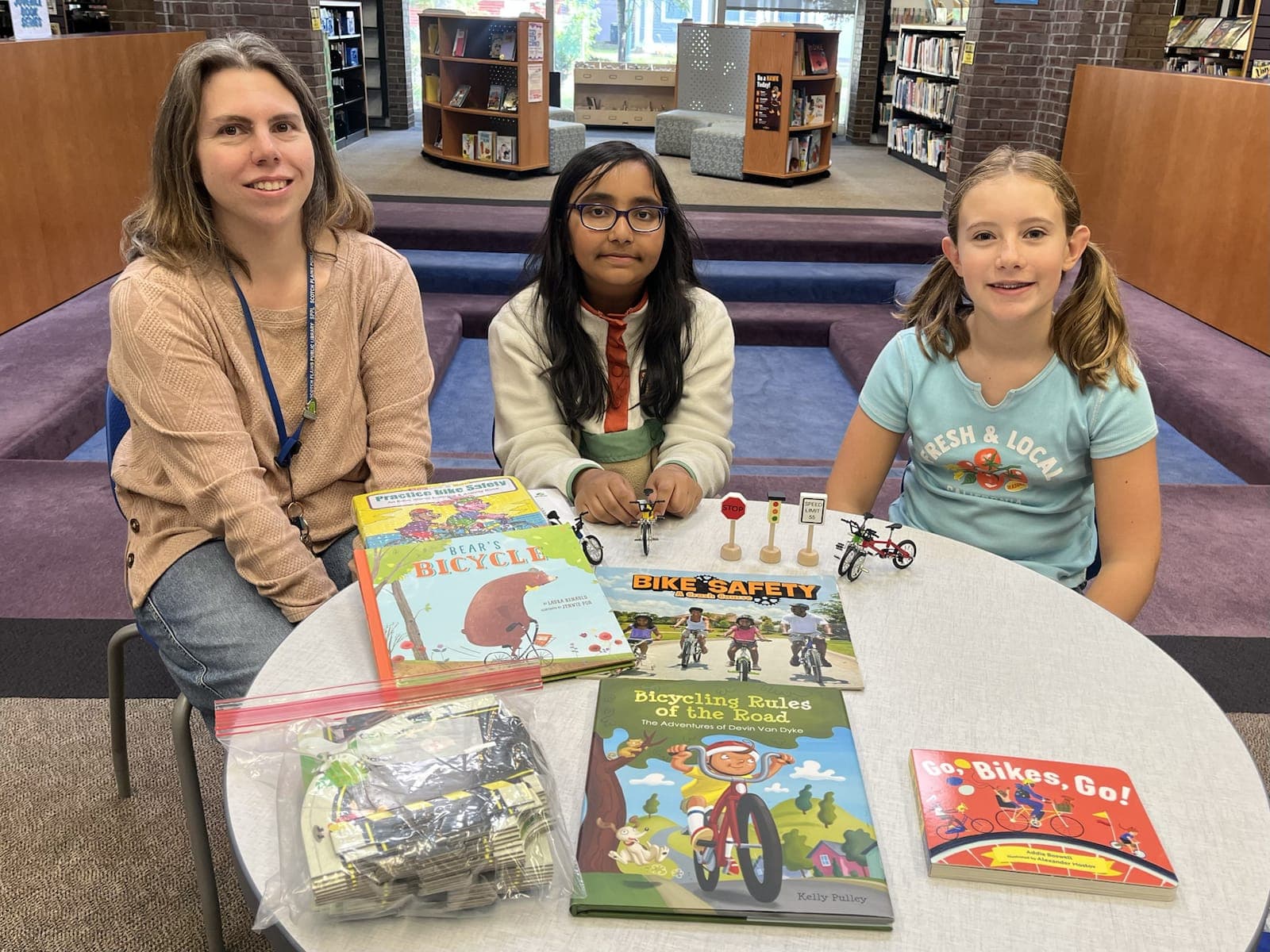 Troop members Eva and Ashley present the Bike Safety Early Literacy Kit to children’s librarian Ms. Lanora.